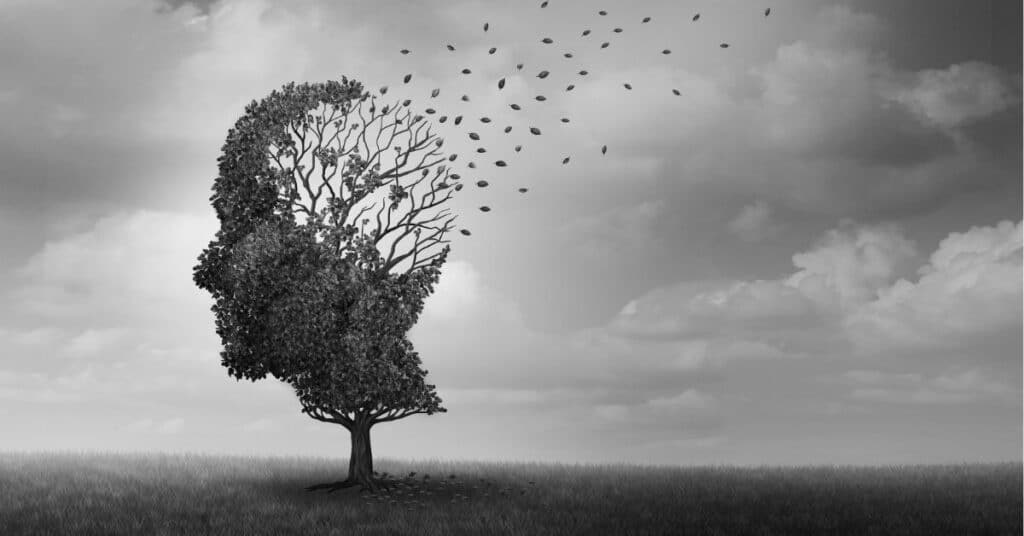 A tree shaped like a human head stands in an open field, with leaves blowing away from the upper branches, symbolizing thoughts or memories drifting away under a cloudy sky.