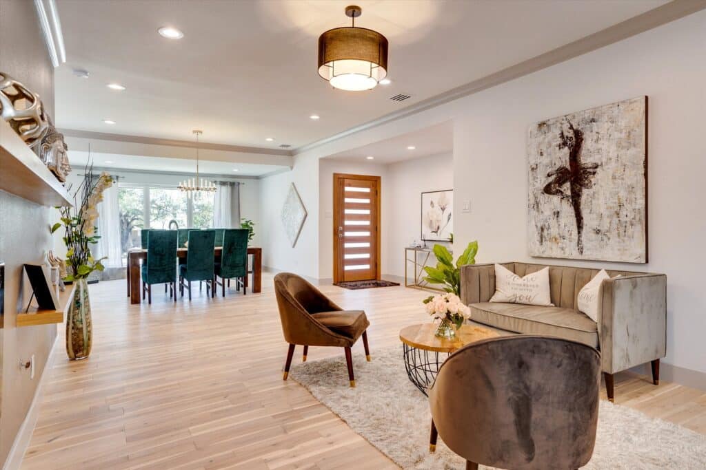 Modern living and dining area with velvet seating, round coffee table, wooden dining table with green chairs, and natural light from large windows.