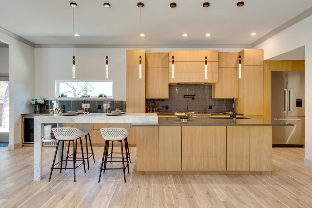 Modern kitchen with light wood cabinets, gray island with black faucet, pendant lights, barstools, and stainless steel stove.