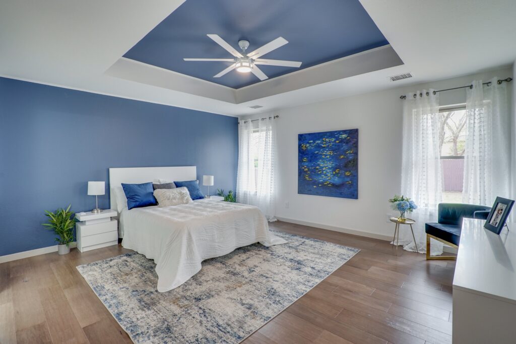 Modern bedroom with white bed, blue accent wall and ceiling, ceiling fan, nightstands, and abstract painting.