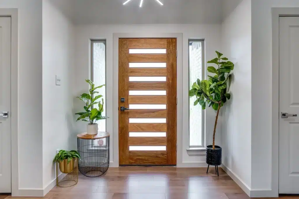 Modern entryway with wooden door, side windows, potted plants, and a small table with decor.