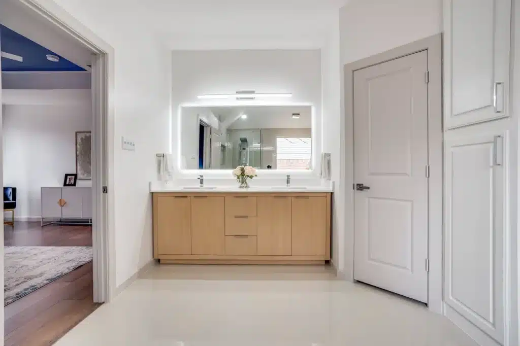 Modern bathroom with double-sink vanity, large mirror, light wood cabinets, and flowers.