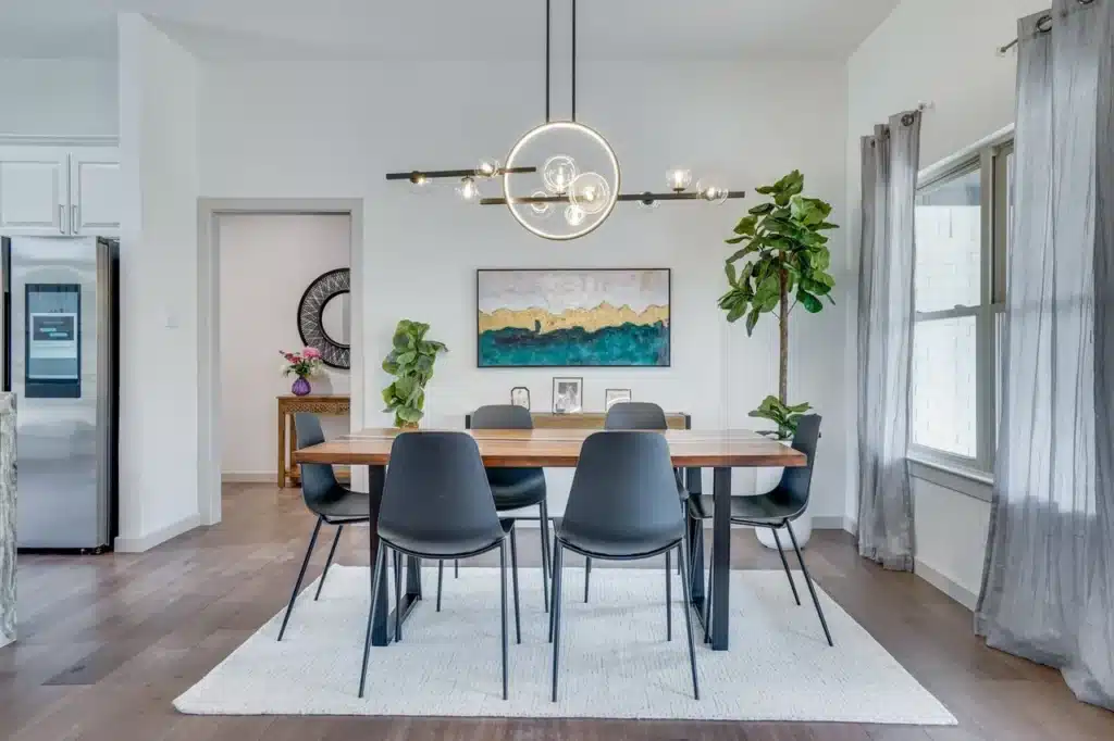 Modern dining room with wooden table, six black chairs, chandelier, abstract painting, and sheer curtains.