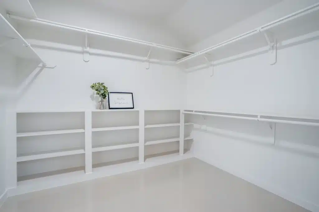 Spacious walk-in closet with white shelves, hanging rods, and decorative vase and sign.