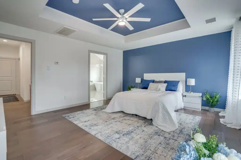 Modern bedroom with blue accent wall and ceiling, white bed with blue pillows, nightstands with lamps, and sheer curtains.