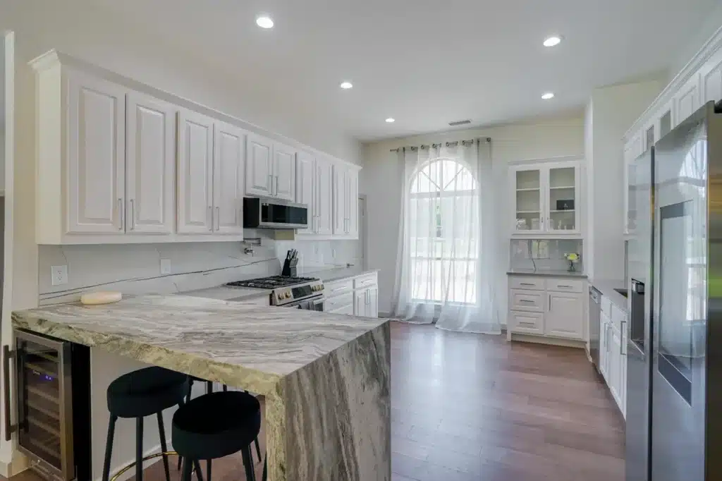 Modern kitchen with white cabinets, marble island, stainless steel appliances, and a large arched window.