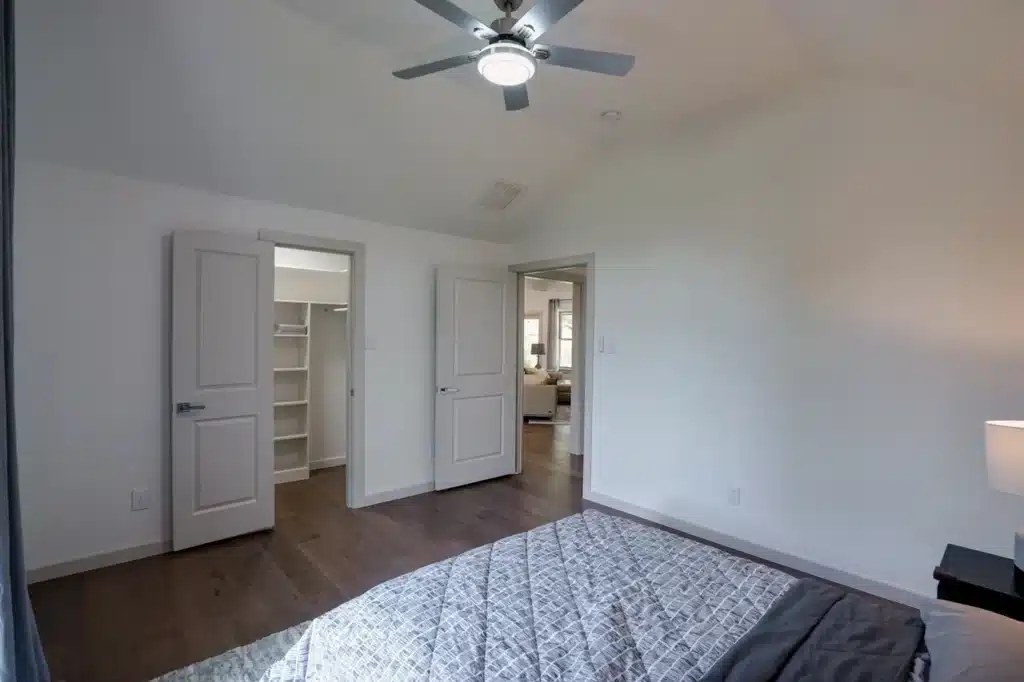 Bedroom with gray patterned bed, ceiling fan, and doors to walk-in closet and living area.