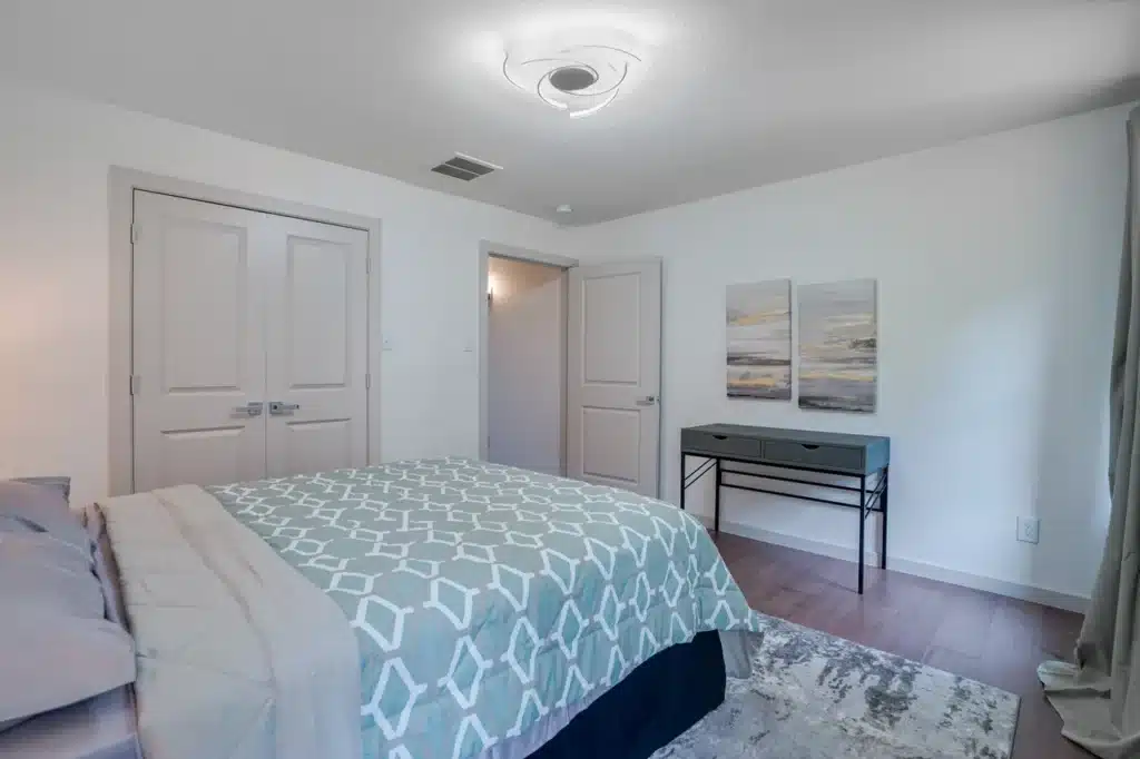 Bedroom with light blue geometric comforter, desk with drawers, abstract wall art, and wooden floor.