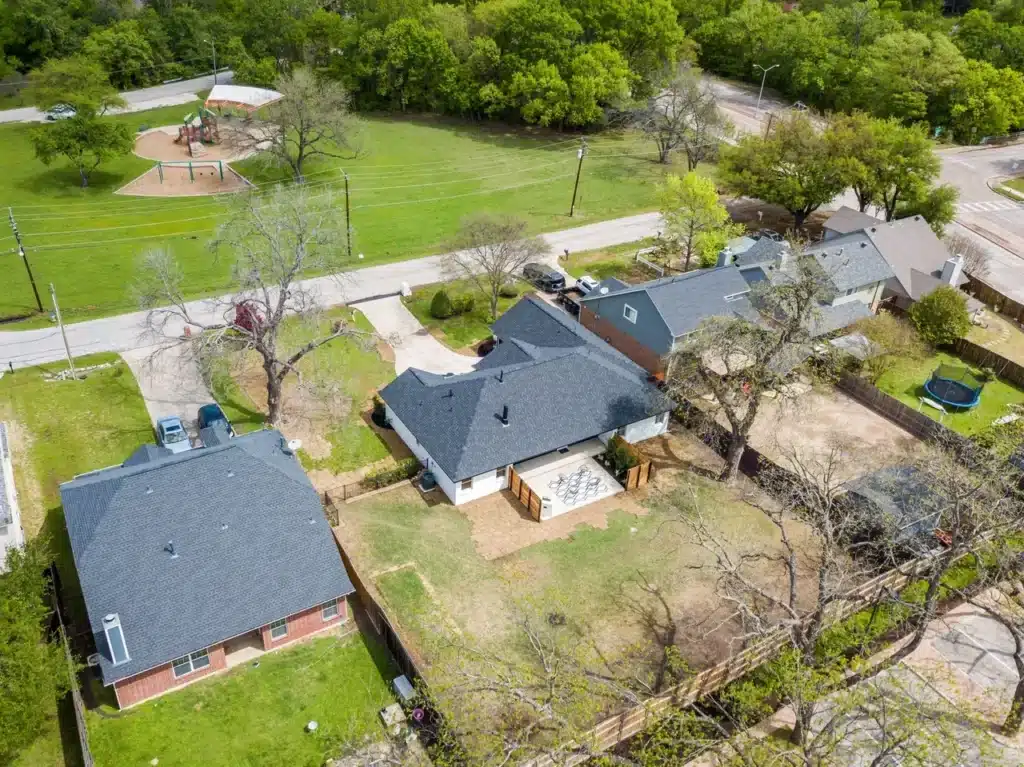 Aerial view of suburban neighborhood with houses, green lawns, trees, and a playground in a nearby park.
