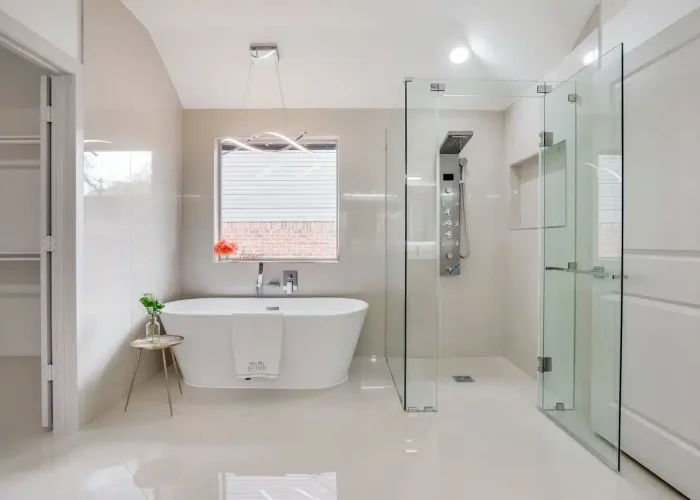 Modern bathroom with freestanding tub, glass shower, side table with plant, and natural light.