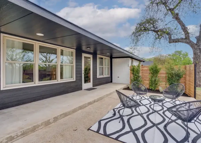 Modern house exterior with black siding, large windows, covered porch, and outdoor seating with a patterned rug.